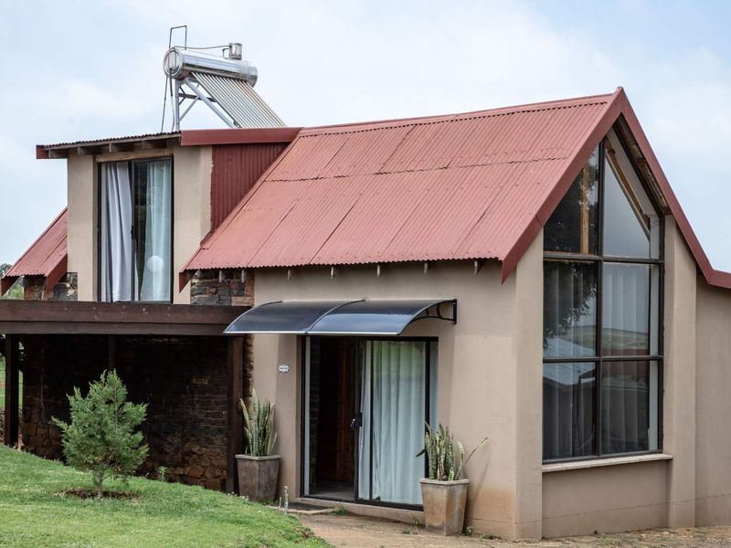 Rear view of a farm-style dwelling featuring a corrugated metal roof, solar water heating system, timber decking, and large glass windows.