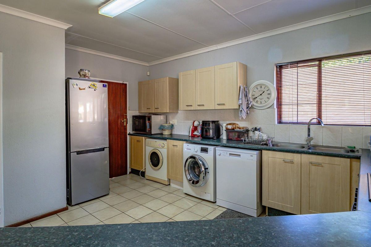 Functional kitchen featuring light wood cabinetry, laminate countertops, tiled flooring, and integrated space for multiple laundry and kitchen appliances.
