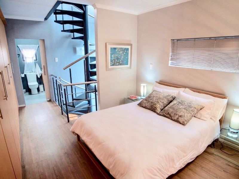 A well-maintained bedroom featuring laminate flooring, built-in cupboards, and a spiral staircase leading to an adjacent bathroom area.
