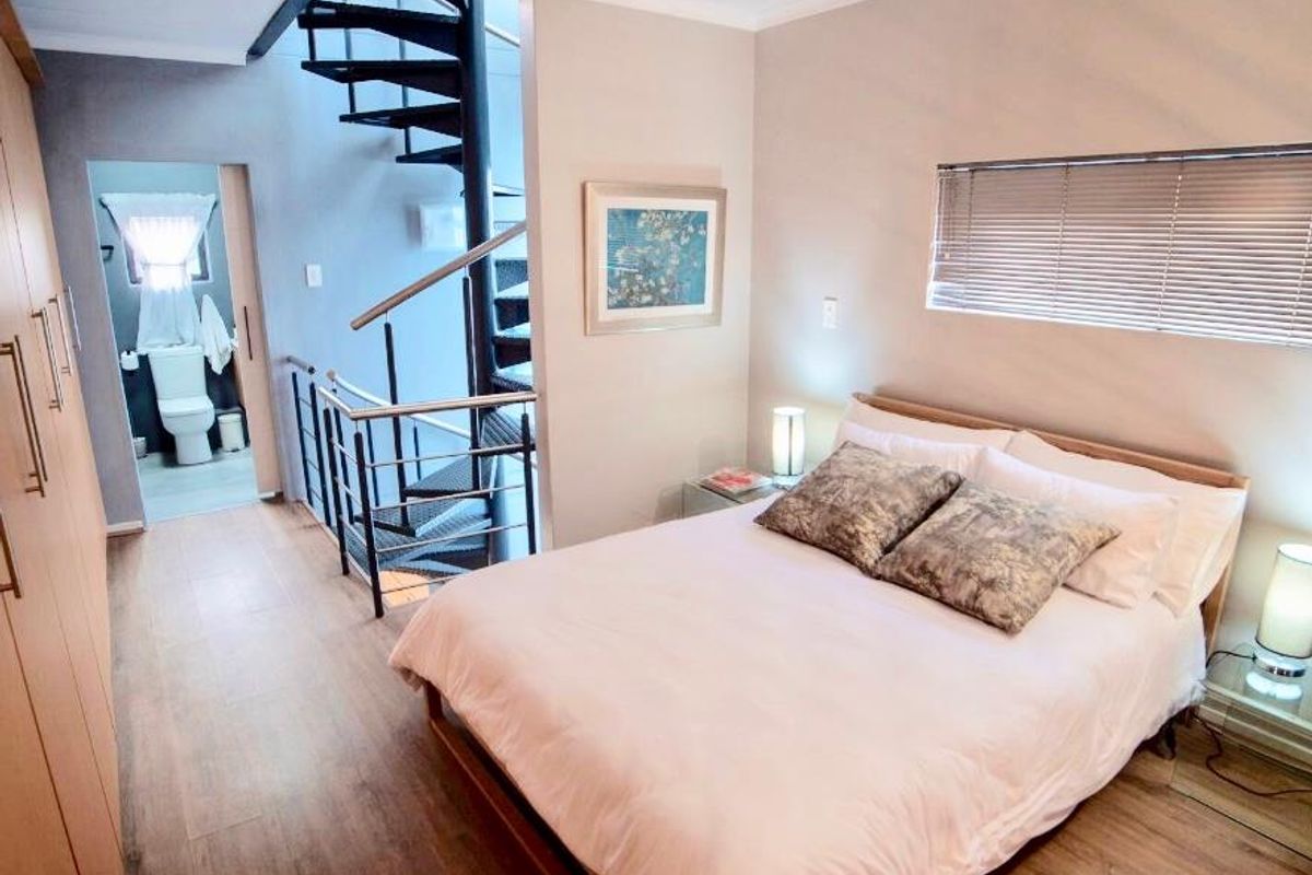 A well-maintained bedroom featuring laminate flooring, built-in cupboards, and a spiral staircase leading to an adjacent bathroom area.