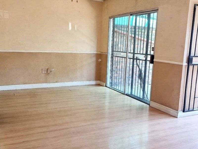 An empty living room featuring laminate flooring, a ceiling fan, and a sliding glass door with an integrated security gate leading to the exterior.
