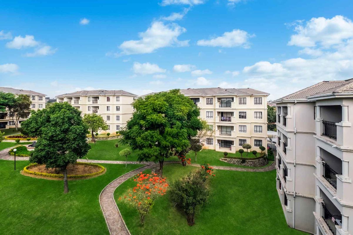 Elevated view of the apartment complex grounds, featuring well-maintained lawns, landscaped garden paths, and mature trees between the residential buildings.
