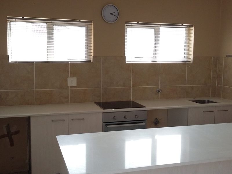 A functional kitchen featuring stone countertops, tiled backsplash, built-in oven and hob, and ample cabinetry, currently awaiting final appliance installation.