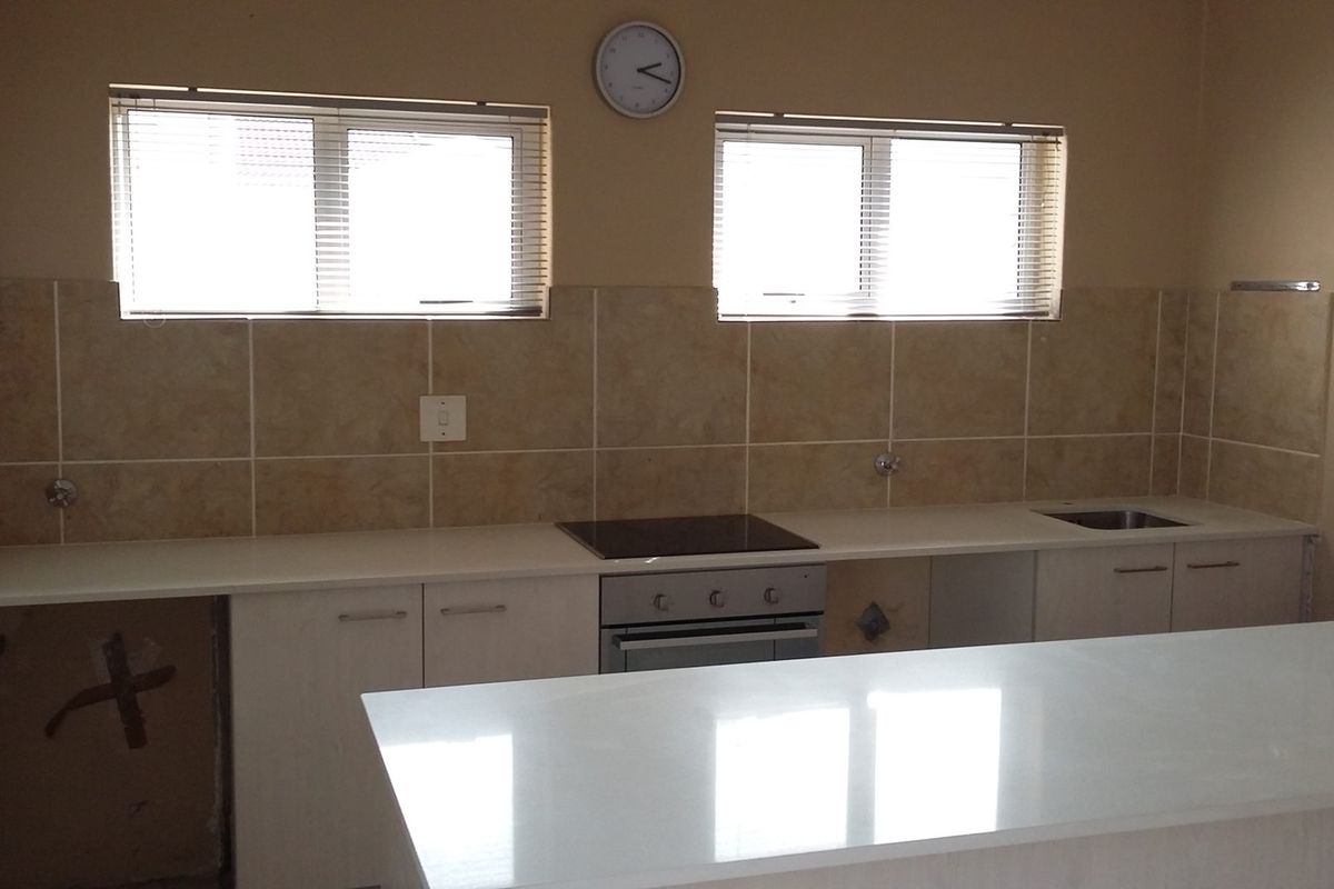 A functional kitchen featuring stone countertops, tiled backsplash, built-in oven and hob, and ample cabinetry, currently awaiting final appliance installation.