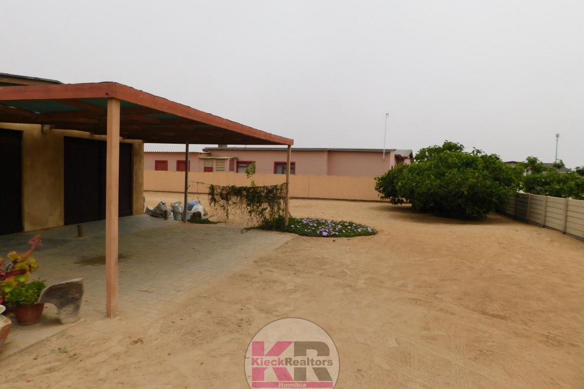 Rear exterior view featuring a covered patio area, perimeter wall, and a large sandy yard space.