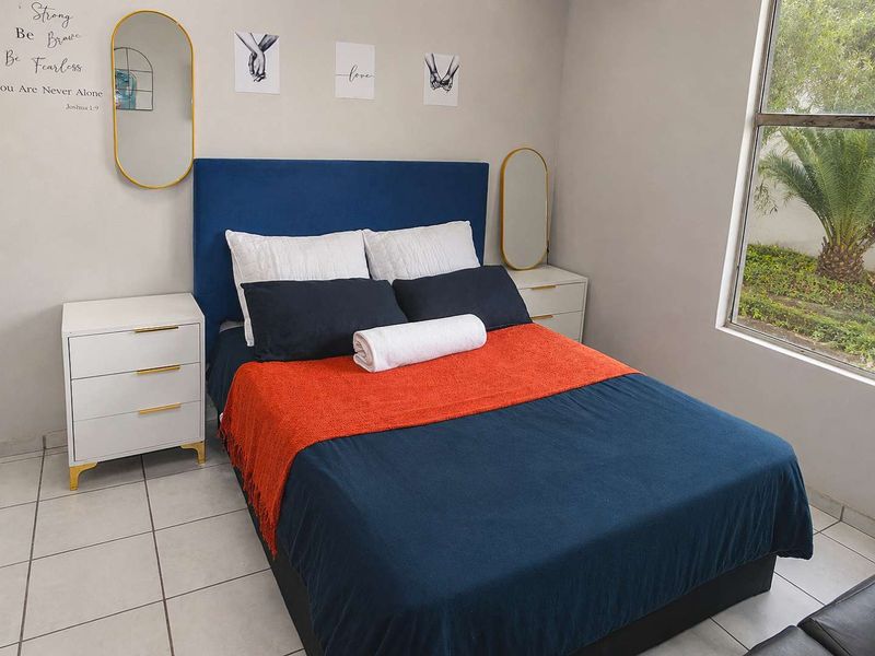 A well-lit bedroom featuring tiled flooring and a large window providing natural light and garden views.