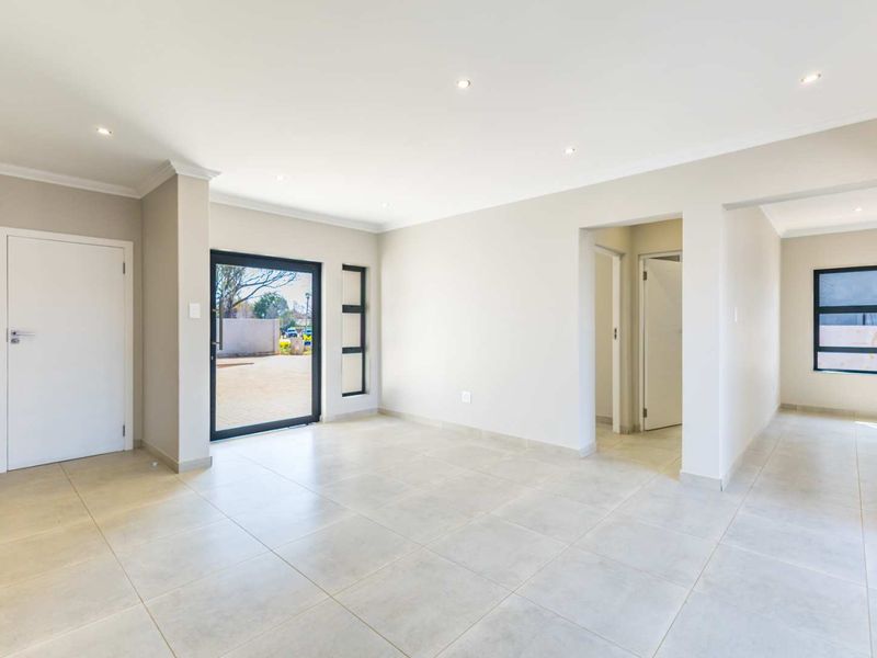 A bright, empty living area featuring neutral tiled flooring, recessed downlights, and modern aluminium-framed doors and windows leading to the exterior.