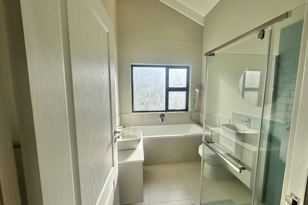 Modern bathroom featuring a built-in bathtub, glass-enclosed shower, vanity basin, and high vaulted ceilings with recessed lighting.