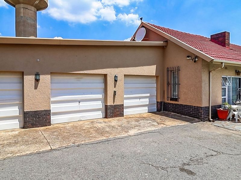 Front exterior view of the property featuring a double garage, tiled roof, and concrete driveway with security features.