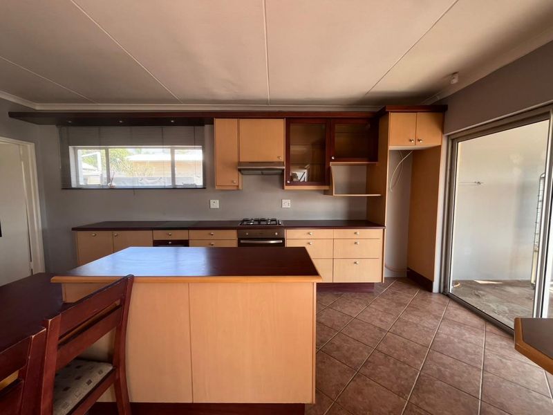Functional kitchen featuring light wood cabinetry, dark laminate countertops, built-in oven and gas hob, tiled flooring, and direct access to the outdoor area.