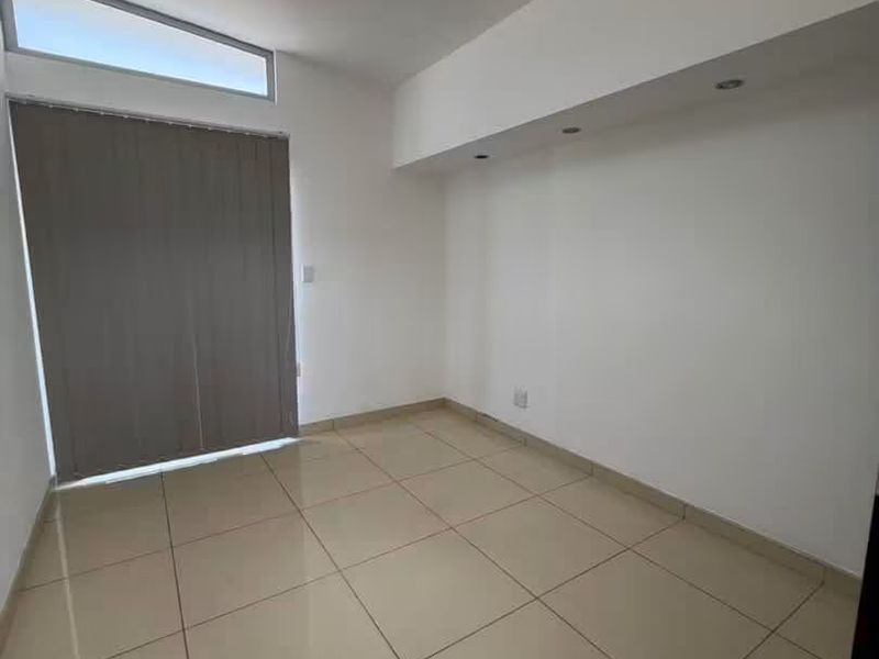 A bright, empty bedroom featuring neutral tiled flooring, recessed ceiling lighting, and a clerestory window with vertical blinds.