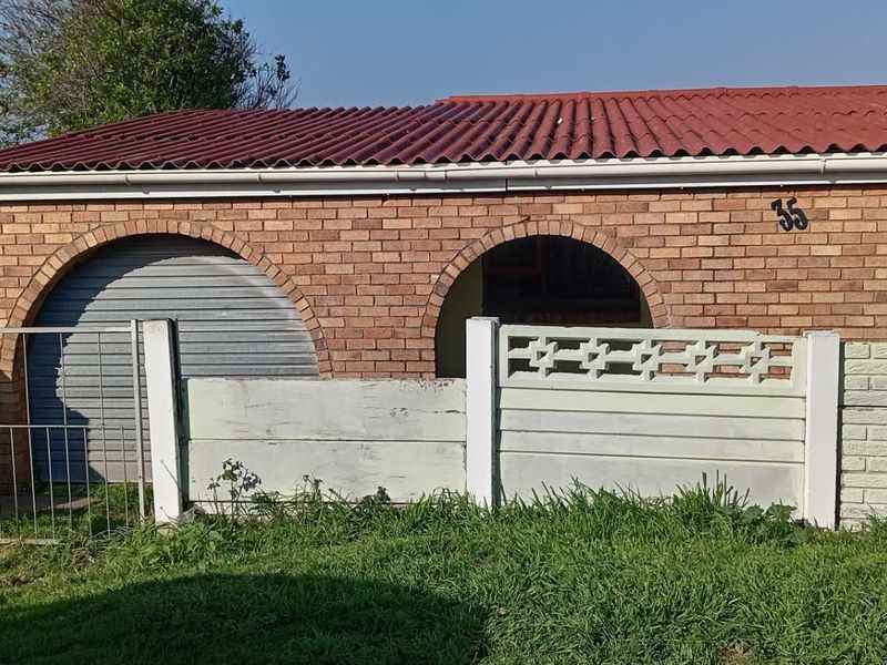 Front elevation of a face brick house featuring arched architectural details, a roller shutter garage door, and a low precast concrete boundary wall.