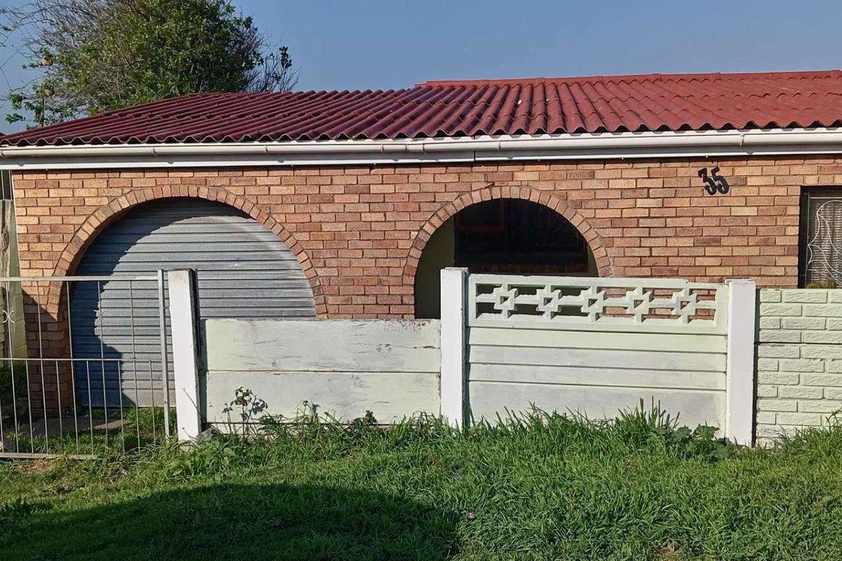 Front elevation of a face brick house featuring arched architectural details, a roller shutter garage door, and a low precast concrete boundary wall.