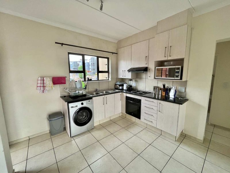 Functional kitchen featuring light-toned cabinetry, dark countertops, tiled flooring, and integrated appliances including an oven, hob, and extractor fan.