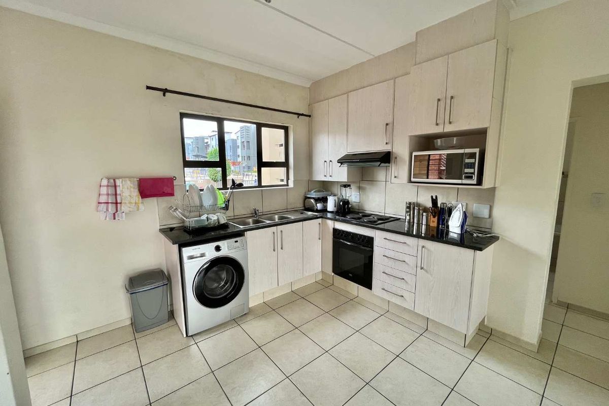 Functional kitchen featuring light-toned cabinetry, dark countertops, tiled flooring, and integrated appliances including an oven, hob, and extractor fan.