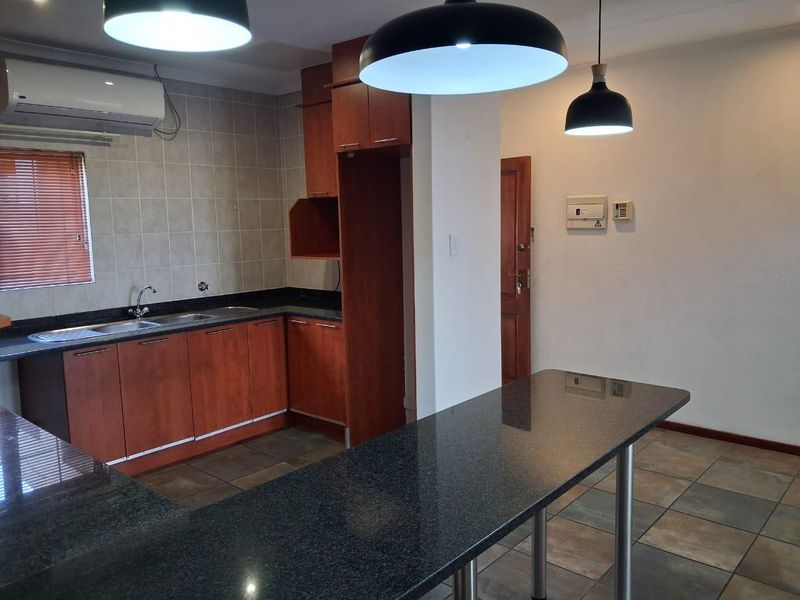 A functional kitchen featuring wooden cabinetry, granite countertops, a breakfast bar, and tiled finishes, offering a clean and practical layout.