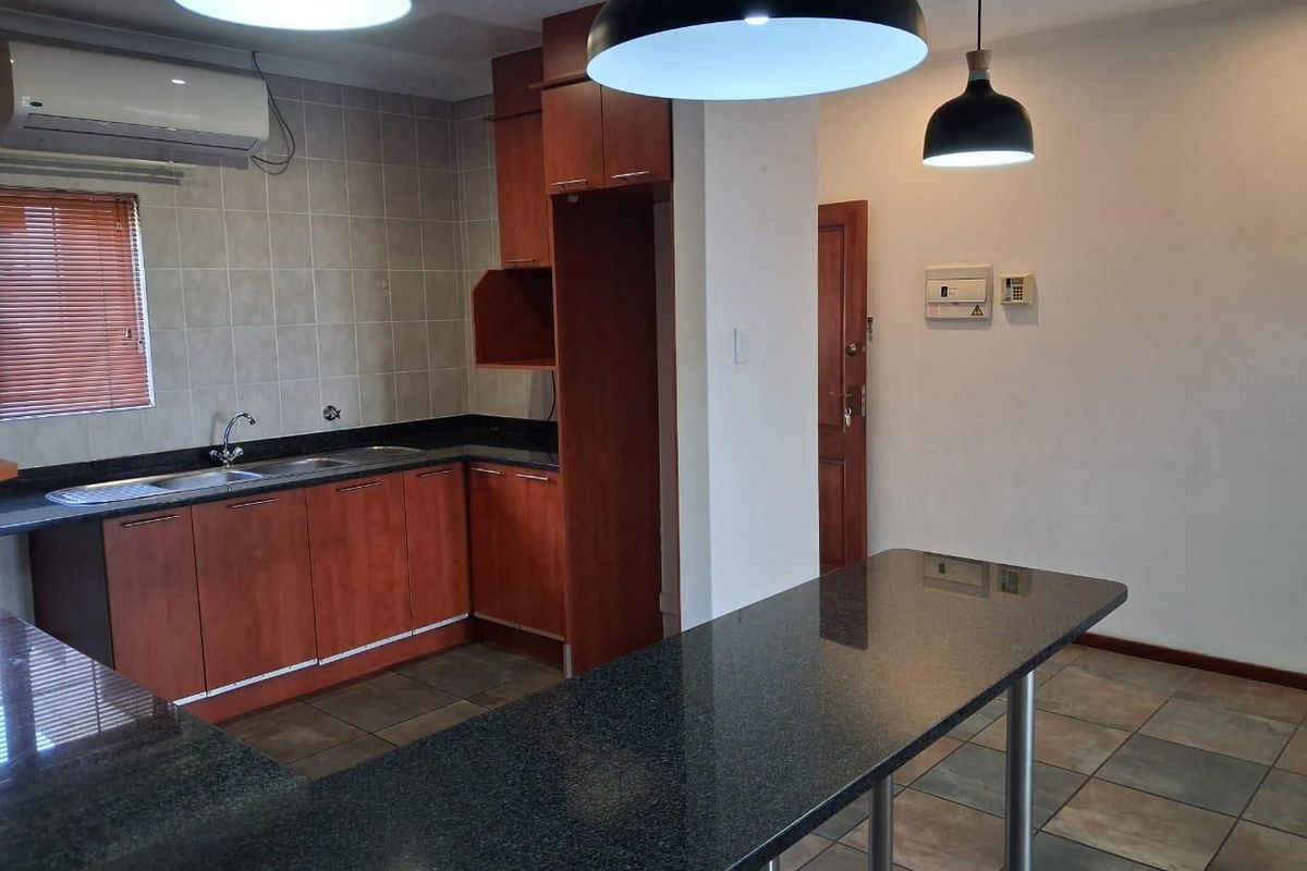 A functional kitchen featuring wooden cabinetry, granite countertops, a breakfast bar, and tiled finishes, offering a clean and practical layout.