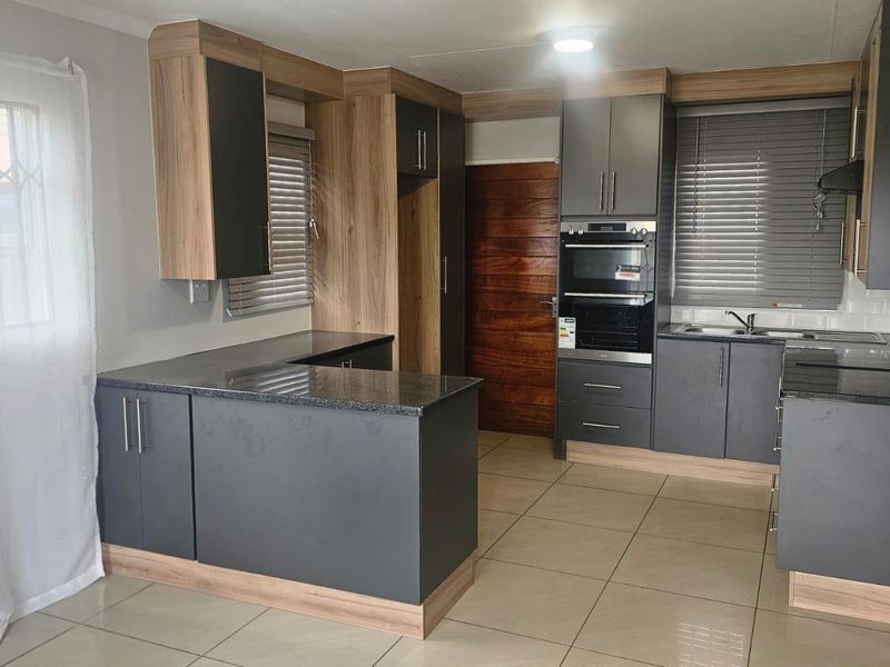 Modern kitchen featuring dark grey cabinetry, wood-look accents, granite countertops, built-in oven, and tiled flooring.