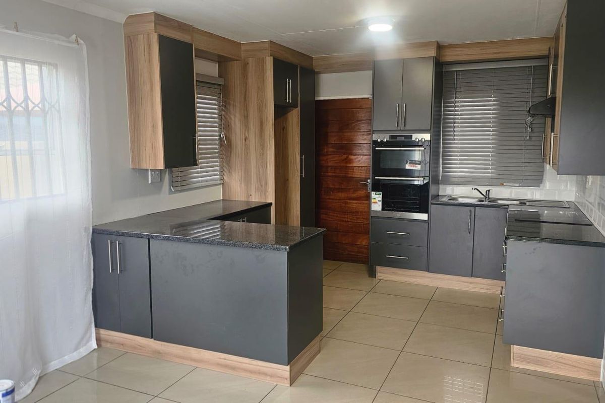 Modern kitchen featuring dark grey cabinetry, wood-look accents, granite countertops, built-in oven, and tiled flooring.