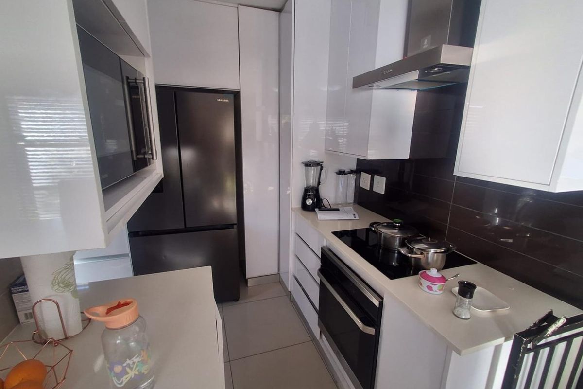 Modern galley-style kitchen featuring sleek white cabinetry, dark tiled splashback, integrated oven, glass cooktop, and stainless steel extractor fan.