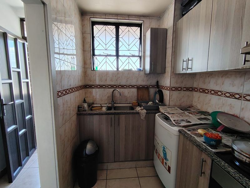Compact kitchen featuring built-in cabinetry, granite countertops, a stainless steel sink, and tiled wall finishes with security bars on the window.