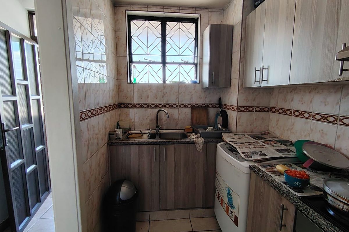 Compact kitchen featuring built-in cabinetry, granite countertops, a stainless steel sink, and tiled wall finishes with security bars on the window.