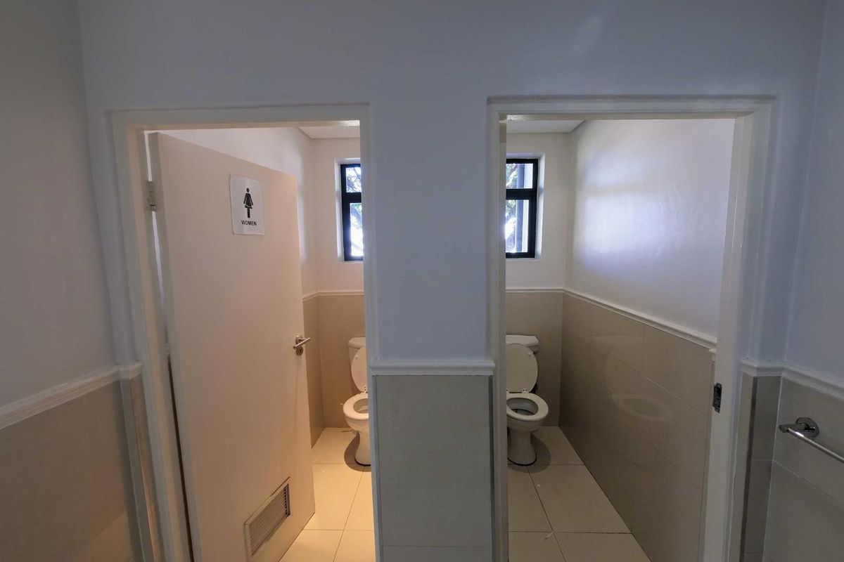 A functional office restroom facility featuring two separate toilet cubicles with tiled walls and modern sanitary fixtures.