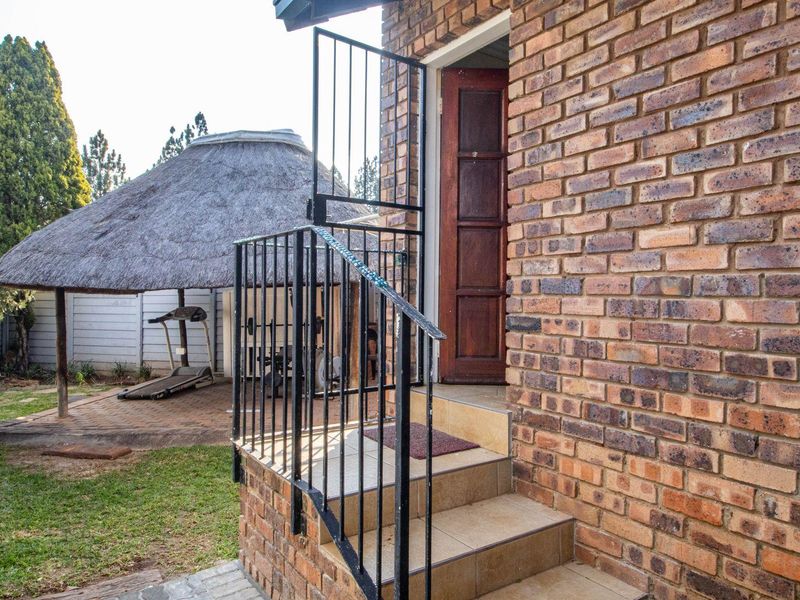 Exterior view of a brick townhouse featuring a tiled entrance staircase with metal security gate and a rear garden with a thatched lapa area.