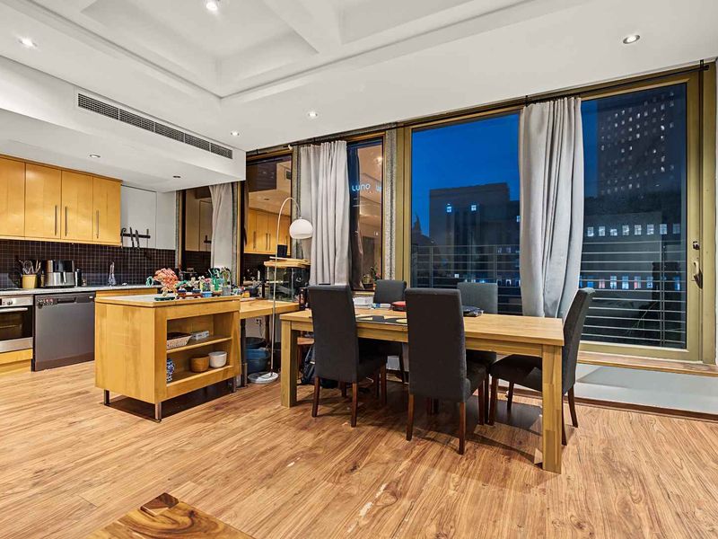 Spacious open-plan kitchen and dining area featuring modern timber cabinetry, integrated appliances, recessed lighting, and large glass doors leading to an outdoor balcony.