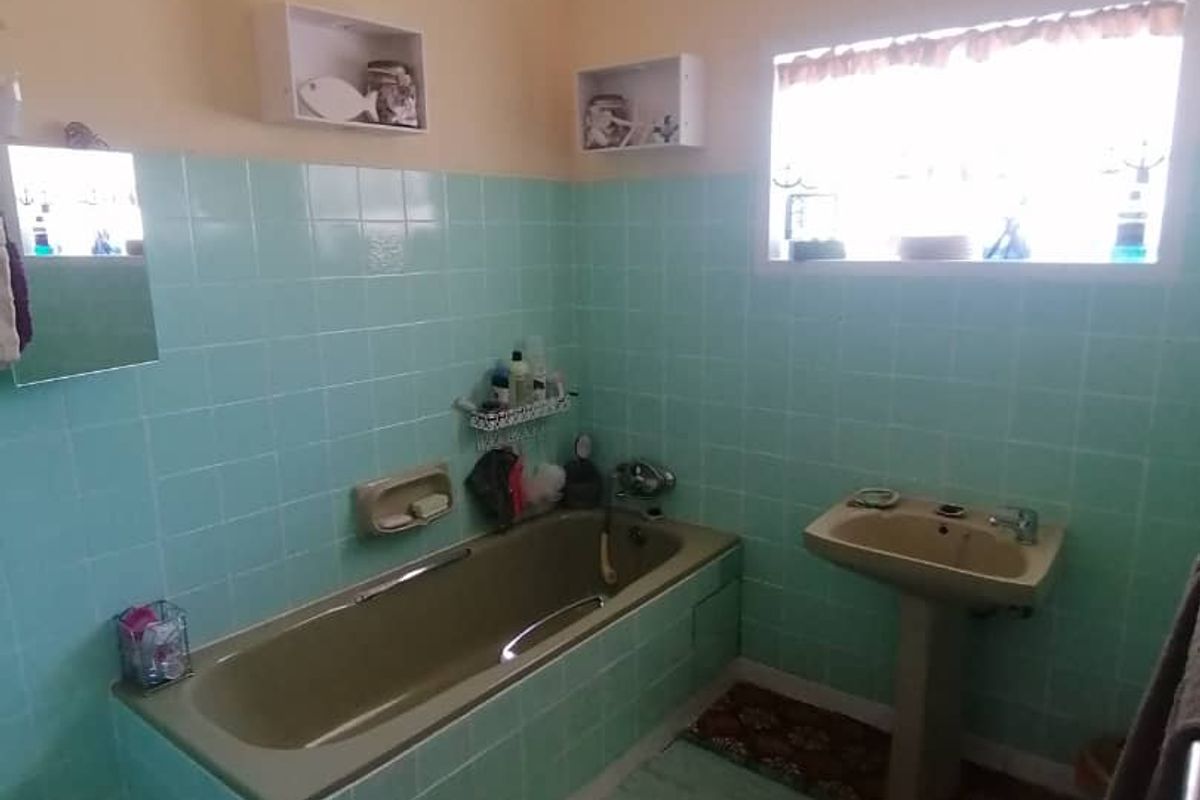 A dated bathroom featuring a built-in bathtub, pedestal basin, and light green wall tiles, offering potential for a modern renovation.