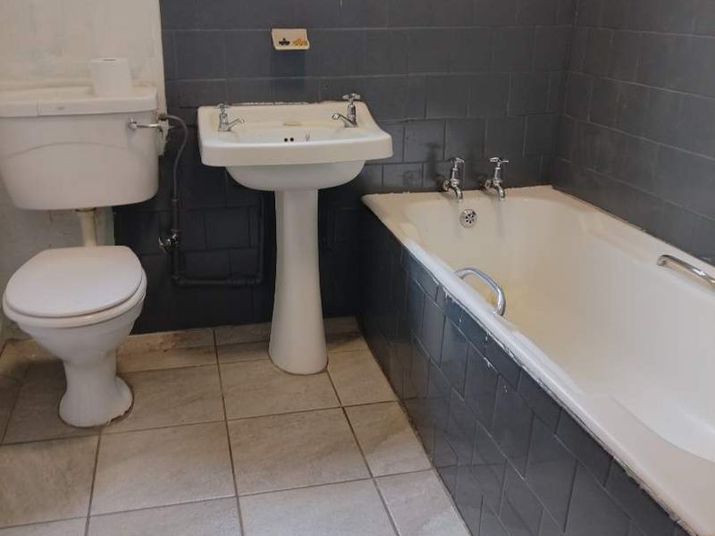 A functional bathroom featuring a pedestal basin, toilet, and bathtub with dark tiled walls and light floor tiles, requiring cosmetic updates and finishing.