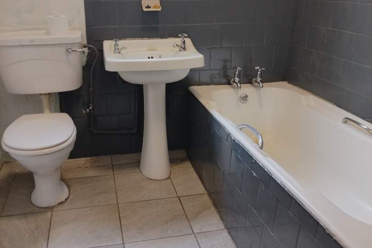 A functional bathroom featuring a pedestal basin, toilet, and bathtub with dark tiled walls and light floor tiles, requiring cosmetic updates and finishing.