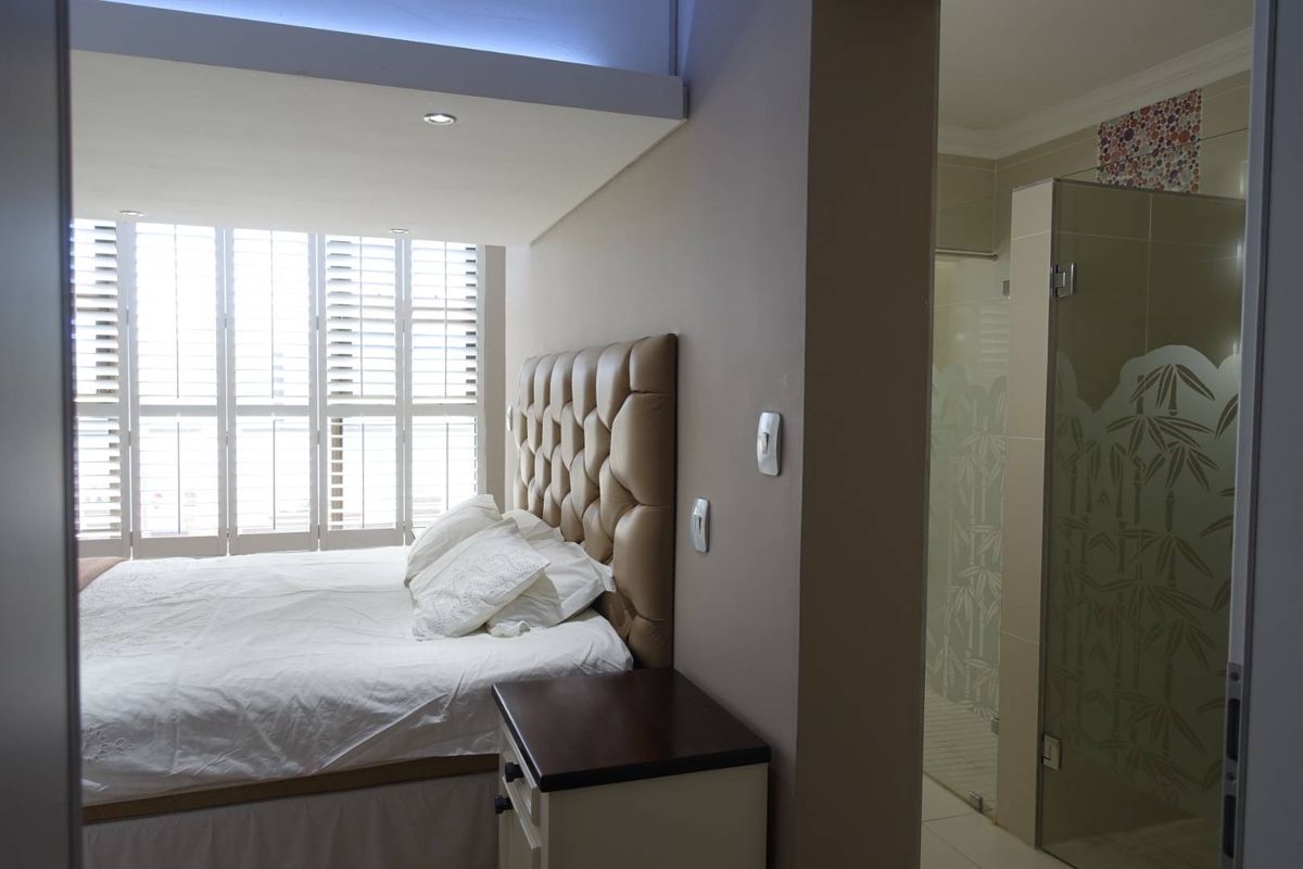 A bedroom featuring plantation shutters and an en-suite bathroom with a glass-enclosed shower and decorative tile accents.