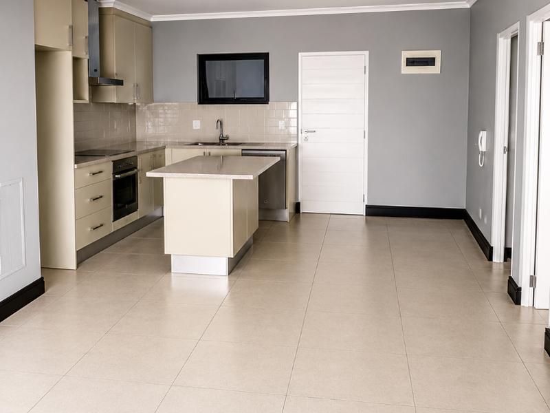 A spacious, modern kitchen featuring neutral cabinetry, a central island, stone countertops, and integrated appliances, finished with clean ceramic floor tiles.