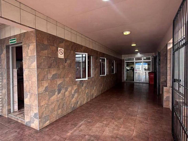 A covered outdoor hallway or walkway featuring tiled flooring and wall cladding, equipped with recessed lighting and metal security gates.