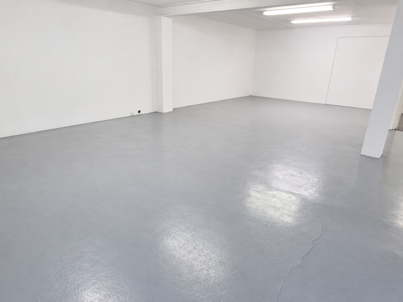 A spacious, open-plan industrial unit featuring a smooth epoxy-coated floor, bright overhead fluorescent lighting, and a clean, neutral white interior finish.