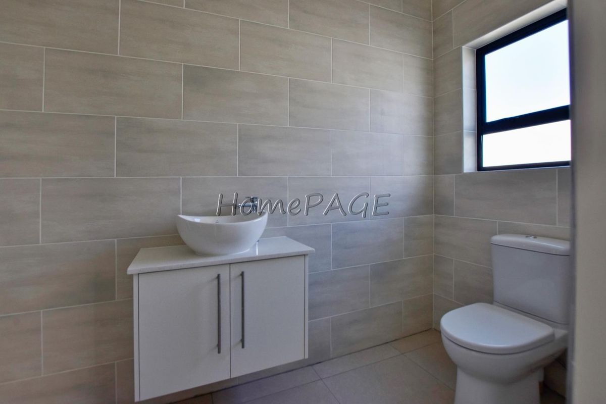 A modern bathroom featuring neutral wall tiles, a floating vanity with a vessel sink, and a standard toilet.