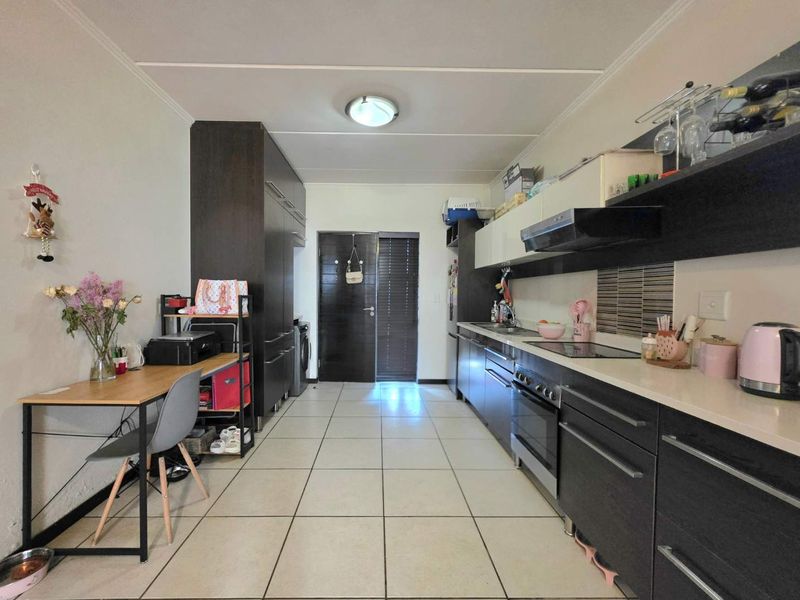 A functional galley-style kitchen featuring dark cabinetry, stone countertops, integrated oven and hob, and tiled flooring throughout.