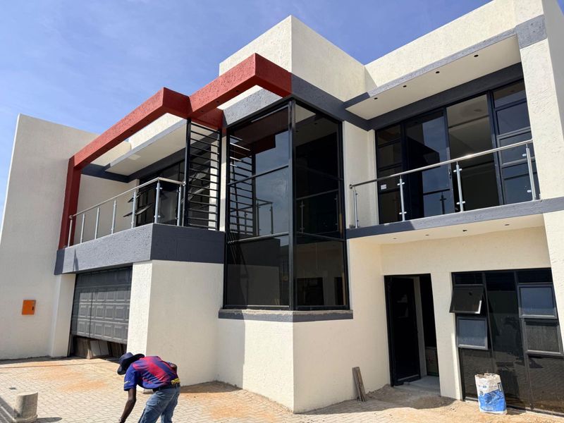 Modern double-storey residential facade featuring clean lines, large glass windows, a balcony with stainless steel balustrades, and an integrated garage.