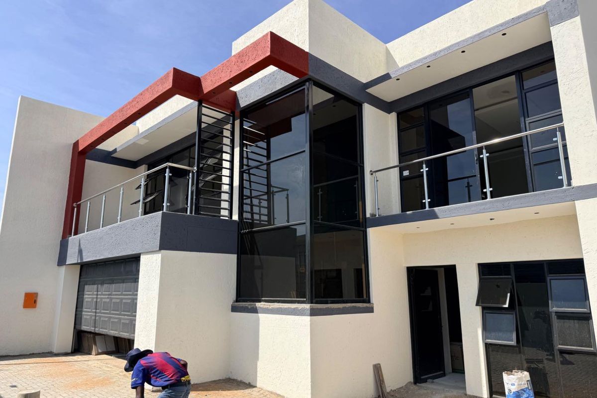 Modern double-storey residential facade featuring clean lines, large glass windows, a balcony with stainless steel balustrades, and an integrated garage.
