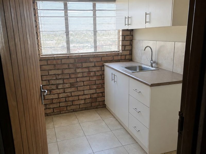 A compact and functional scullery featuring exposed brick walls, tiled flooring, built-in white cabinetry, and a stainless steel sink.