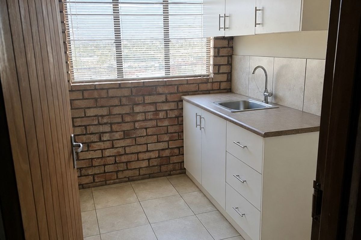 A compact and functional scullery featuring exposed brick walls, tiled flooring, built-in white cabinetry, and a stainless steel sink.