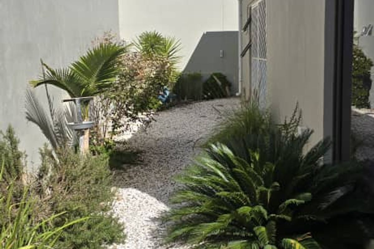 A side garden area featuring gravel landscaping, artificial turf, and perimeter electric fencing along the property boundary.