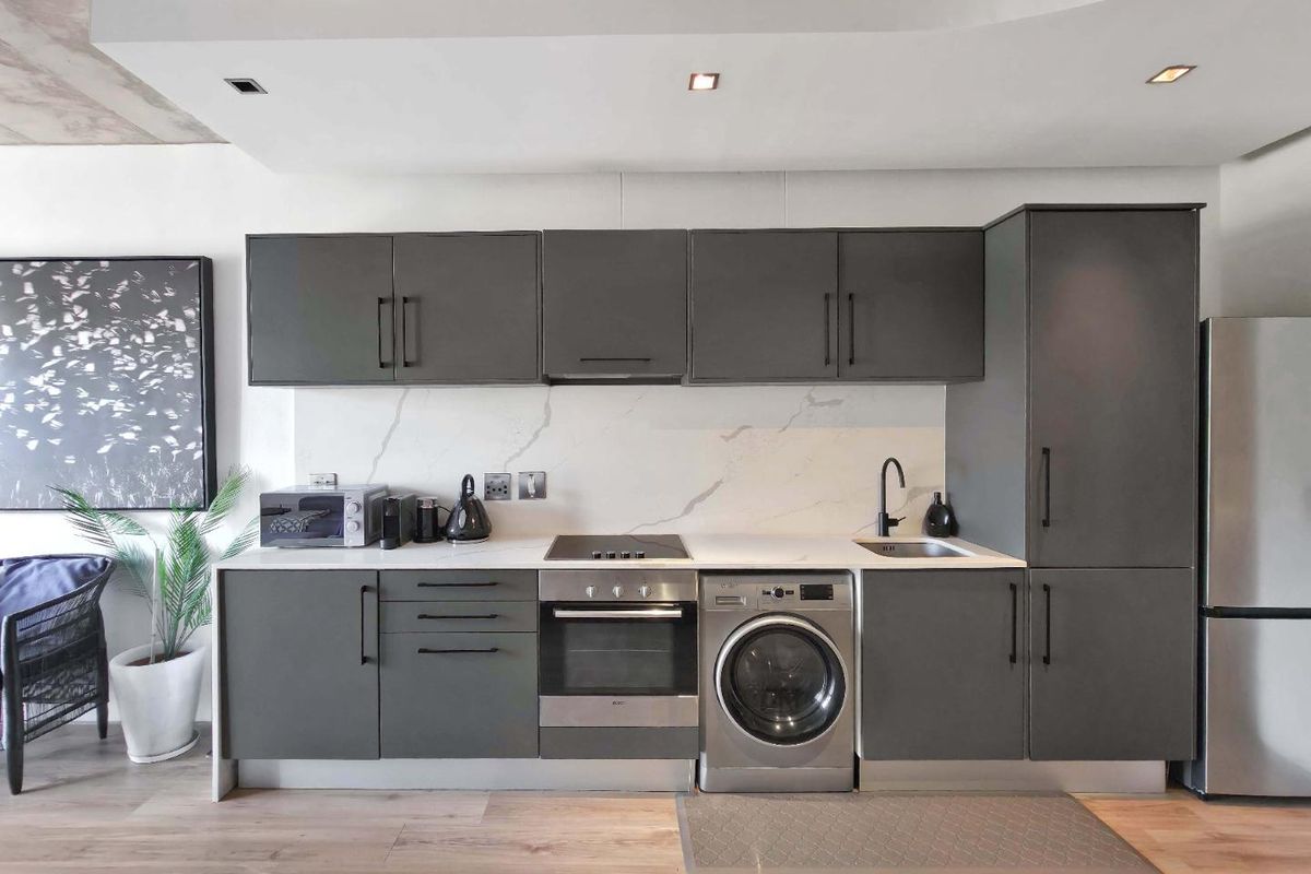 Modern kitchen featuring sleek dark grey cabinetry, stone-look backsplash, integrated oven, electric hob, and recessed ceiling lighting in an open-plan layout.