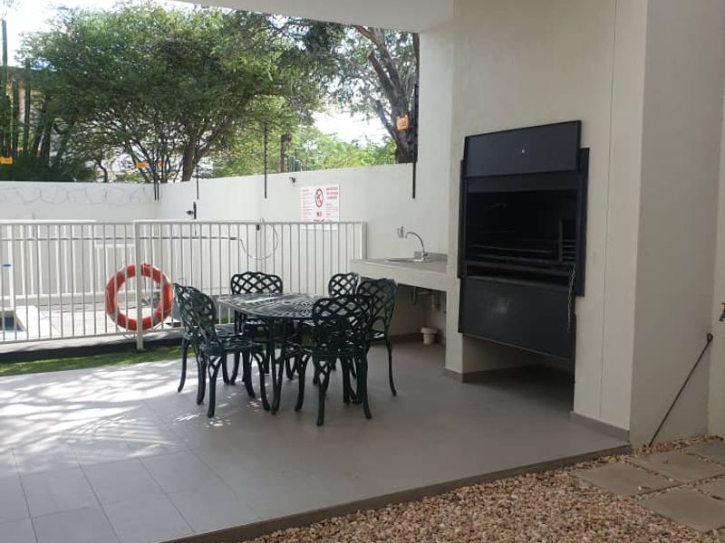 Covered patio area featuring a built-in braai, prep sink, and tiled flooring, overlooking a gravel garden and pool area.