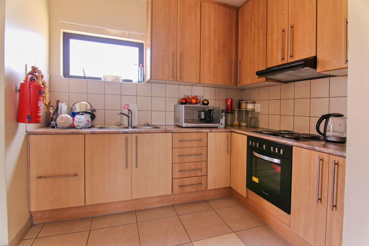 A functional kitchen featuring light wood cabinetry, tiled splashbacks, a built-in oven, hob, and extractor fan with a double sink.