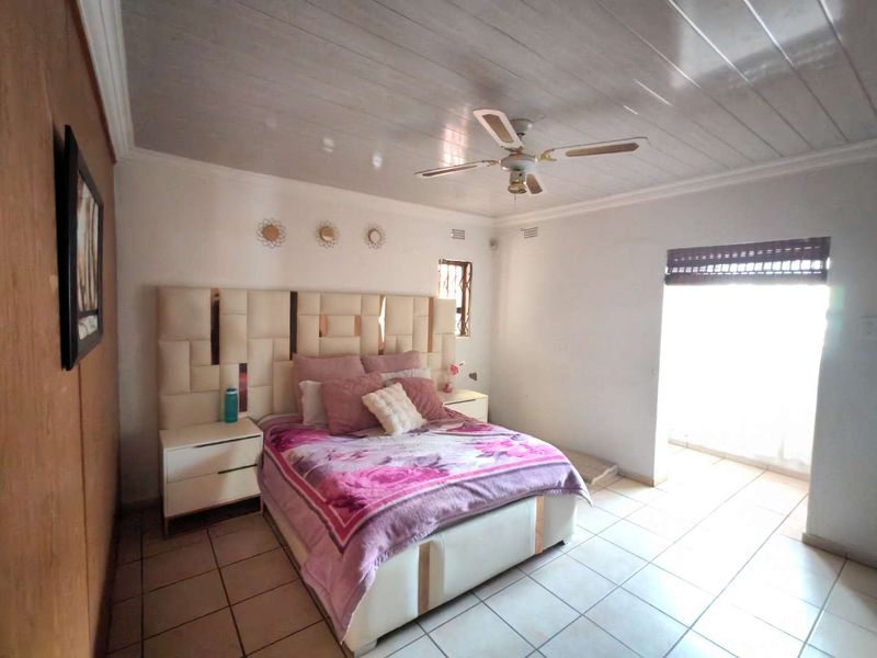 A bedroom featuring tiled flooring, a ceiling fan, and timber-look ceiling panels, with access to an outdoor area through a security gate.