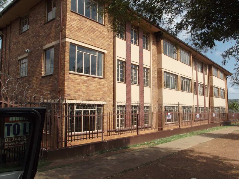 Exterior view of a multi-story apartment building featuring a face brick facade, steel-framed windows, and perimeter security fencing with razor wire.
