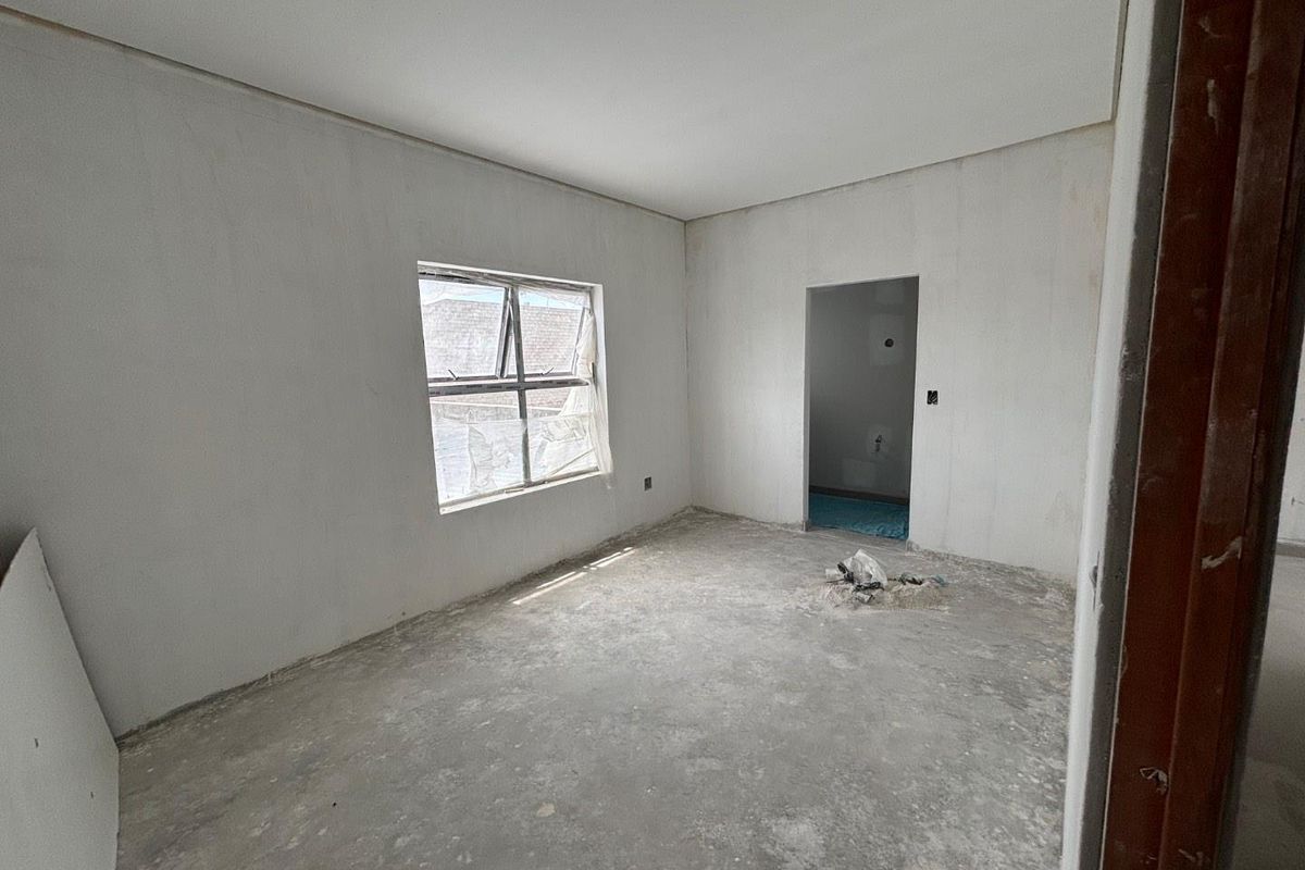 An unfinished bedroom space featuring plastered walls, a concrete floor, and an aluminium window frame, currently in a construction phase.