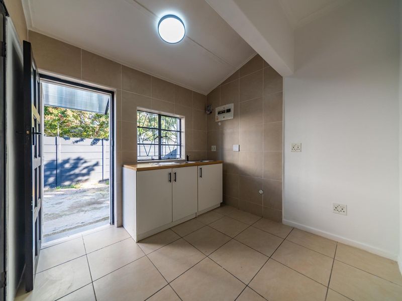 A clean and functional laundry area featuring tiled flooring, built-in base cabinetry with a sink, and direct access to the exterior.